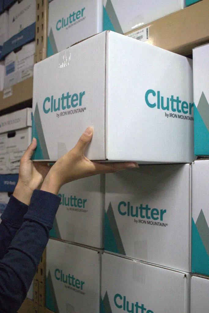 Hands placing a Clutter by Iron Mountain box in a secure warehouse
